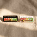 Colorful enamel pin featuring a funny social battery design, shown on a clean neutral background